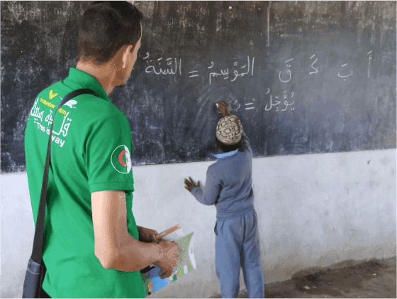 A Sabili Foundation member overseeing a young student writing Arabic on the board