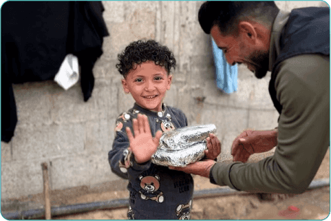 A joyful displaced Palestinian child smiles with gratitude while receiving a hot meal