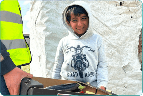 A displaced Palestinian child filled with joy as he receives a box of vegetables